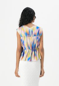 Farbige Bluse mit angeschnittenen Ärmeln, die ein Batikmuster in Pink, Blau und Gelb zeigt, mit gerafftem Taillenbereich und weichem, leichtem Stoff.