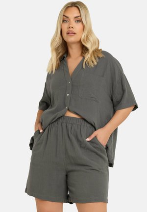 Completo grigio a due pezzi composto da una camicia a maniche corte con bottoni e tasca sul petto, abbinata a pantaloni corti con vita elastica. Tessuto strutturato.