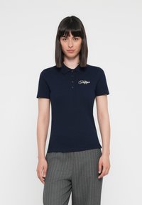 Polo navy de algodón con cuello clásico, que presenta un logo bordado en dorado en el lado izquierdo del pecho y mangas cortas.