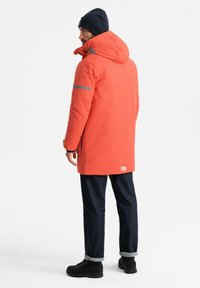 Heldere oranje geïsoleerde jas met capuchon en reflecterende streep, gecombineerd met donkere spijkerbroek en zwarte laarzen. Minimalistische designdetails.