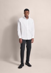 Weißes Hemd mit langen Ärmeln, kombiniert mit dunkelgrauen, taillierten Hosen und schwarzen Schuhen. Glattes Material mit einem strukturierten Design.