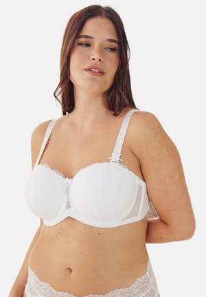 Woman with medium skin tone and brown hair wearing a white lace bra and matching lace underwear, looking to the side against a plain background.