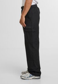 Schwarze Cargo-Hosen mit lockerer Passform, elastischem Taillenbund, Seitentaschen und glatter Textur. Mit Nähdetails und geradem Beindesign.