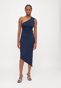 Robe bleu marine à une épaule avec un ourlet asymétrique, en tissu extensible, présentant une découpe sur le côté et une silhouette ajustée.