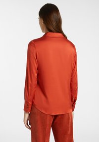 Camicia in satin rosso con maniche lunghe e colletto. Caratterizzata da polsini con bottoni e una texture liscia e lucida.