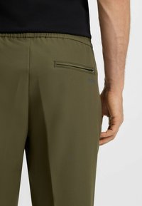 Olivgrüne Jogginghosen aus glattem Stoff mit einem elastischen Bund und einer Reißverschlusstasche auf der Rückseite. Mit einem dezenten "BOSS"-Logo.