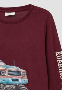 Burgunderfarbendes Langarmshirt mit einem Grafikdruck eines blauen Trucks. Verfügt über einen gerippten Halsausschnitt und einen in Weiß bedruckten Text "ROARING" auf dem Ärmel.