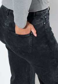 Jean en denim noir avec une texture déchirée et une poche arrière. Dispose d'une taille haute et de subtils accents en métal.
