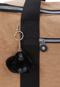 Borsa di tessuto marrone con una tracolla nera, caratterizzata da dettagli in zip argentati. Un portachiavi a forma di gorilla nero pende dalla tracolla.