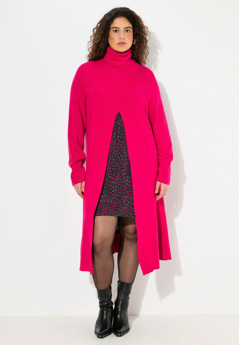 Robe pull longue fuchsia avec un col roulé, comportant une fente à l'avant qui dévoile une robe noire à motif floral ; portée avec des bottines noires.
