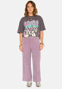 T-shirt graphique gris surdimensionné avec un design AC/DC ; pantalon large en velours côtelé lavande ; baskets grises ; bracelets en or superposés.