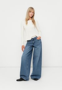 Wide-leg blue denim jeans with a smooth texture, paired with a cream long-sleeve sweater. The outfit has an organic, relaxed silhouette.