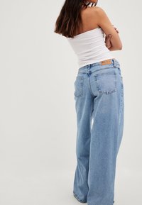 Jasnoniebieskie, wysokie dżinsy o szerokich nogawkach z luźnym krojem, z dwoma tylnymi kieszeniami i markową, brązową skórzaną metką w pasie.