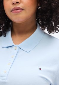 Ανοιχτό μπλε πόλο με υφασμάτινη υφή, διαθέτει κλασικό γιακά και τρία κουμπιά. Σημαντικό έμβλημα λογότυπου στην αριστερή πλευρά.