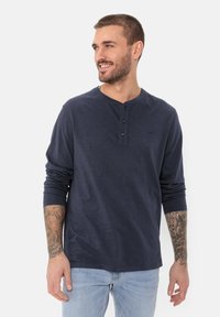 Navyblaues Langarm-Henley-Shirt mit einer Dreiknopfleiste, rundem Ausschnitt und weicher Textur, kombiniert mit hellblauen Jeans.