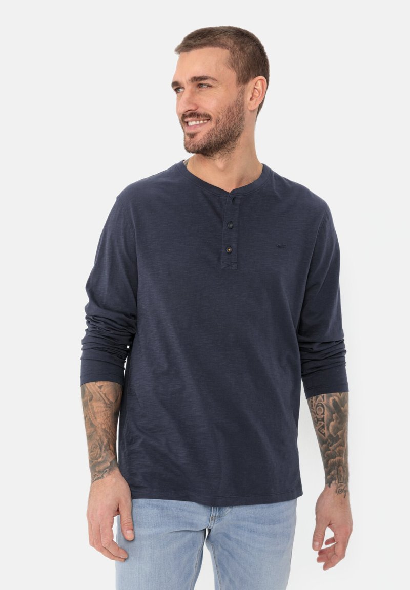 Navyblaues Langarm-Henley-Shirt mit einer Dreiknopfleiste, rundem Ausschnitt und weicher Textur, kombiniert mit hellblauen Jeans.