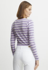 Randig långärmad topp i lavendel och vitt, gjord av mjukt tyg. Har rund halsringning och figurnära design, kombinerad med vita jeans.