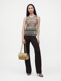 Femme portant un haut sans manches à motif zigzag multicolore et un pantalon noir à motif zigzag, tenant un sac à main zigzag multicolore avec des anses en chaîne dorée.