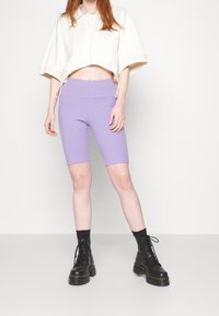 Ljusfärgad kort topp med vida ärmar, matchad med tajta lavendelfärgade cykelbyxor. Svarta ankelstövlar med tjocka sulor.