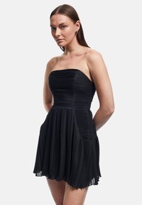 Strapless zwart jurk met geplooide textuur, uitlopende rok en zijzakken. De stof heeft een subtiele glans, die het ontwerp versterkt.