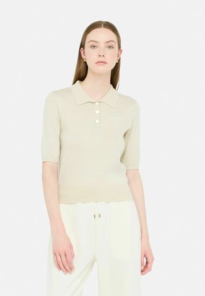 Polo maglietta beige a maniche corte con colletto, caratterizzata da quattro bottoni e un tessuto leggermente strutturato, abbinata a pantaloni bianchi.