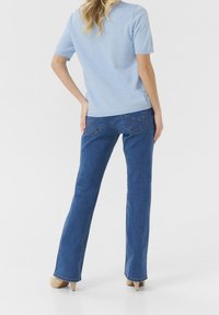 Himmelblaues Kurzarmpullover mit strukturierten Punkten, kombiniert mit dunkelblauen Schlagjeans und nudefarbenen Absätzen, von hinten gezeigt.