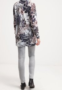 Camicia a maniche lunghe con stampa floreale in tonalità scure e chiare, abbinata a jeans skinny grigi e stivaletti neri.
