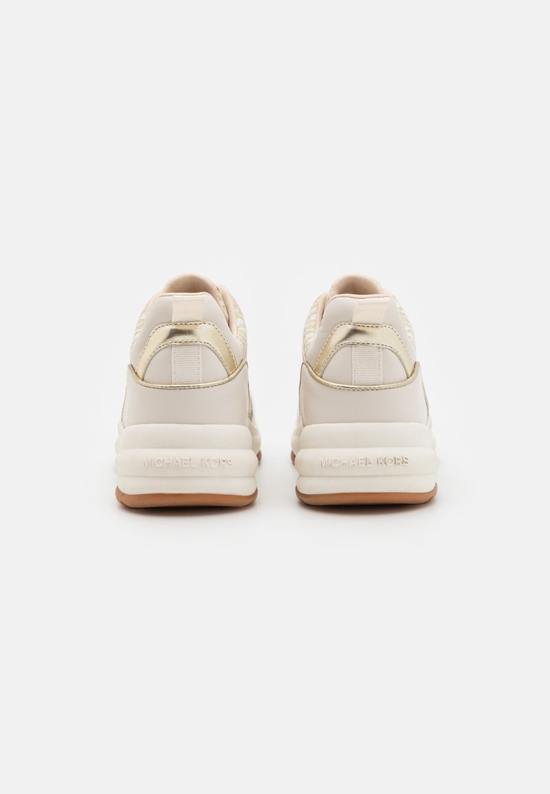 Un par de zapatillas Michael Kors en beige y dorado vista desde atrás, con suelas blancas gruesas y suelas externas marrones sobre un fondo blanco.