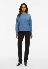 Blå fleecetröja med "TRUTH" broderi på bröstet, kombinerad med svarta raka jeans och svarta klackstövlar.