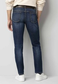 Donkerblauwe denim jeans met een slim fit, voorzien van twee achterzakken en een bruine riem. Gekoombineerd met witte sneakers.