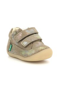Zapatos de bebé beige con parte superior de tela texturizada, dos correas de Velcro y suela de goma. Presentan un sutil patrón floral y una etiqueta de logo verde.