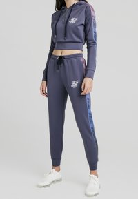 Námořnicky modrá zkrácená mikina s kapucí na zip a logem, doplněná o odpovídající tepláky s vícebarevnými bočními akcenty a stahovací šňůrkou v pase.