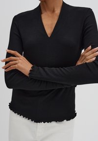 Zwarte geribbelde longsleeve top met een diepe V-hals, voorzien van gerimpelde randen bij de mouwen en onderzijde voor extra textuur en detail.