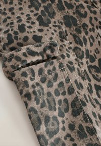 Materiał w leopardzie cętki w kolorze beżowym i ciemnozielonym, z teksturowaną powierzchnią i prostym krojem, z dodatkowymi kieszeniami na mankietach.