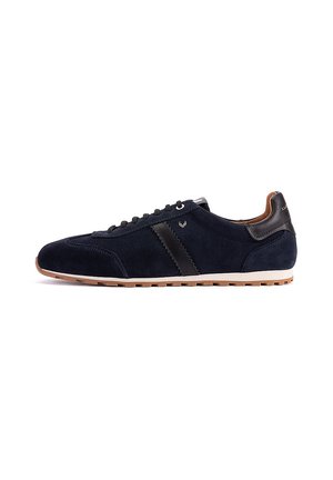 Zapatilla deportiva de ante azul marino con detalle de cuero negro, forro interior marrón, suela blanca y suela exterior de goma, vista lateral.