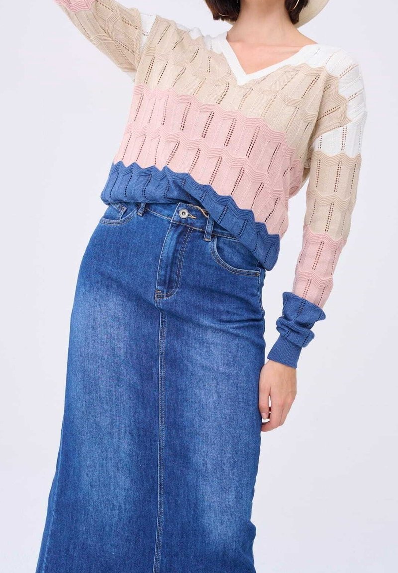 Femme portant un pull en maille à motif chevron beige, rose et bleu, assorti d'une jupe en jean bleu taille haute.