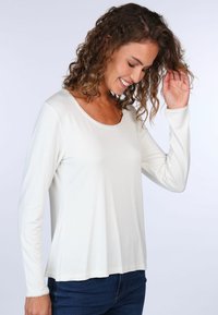 Langärmliges, cremefarbenes Oberteil mit Rundhalsausschnitt und Spitzenbesatz entlang der Kanten, aus weichem, leichtem Stoff gefertigt.