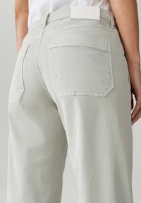 Pantaloni grigi chiari a vita alta con tasche cucite e una texture liscia. Presentano un'etichetta bianca del marchio sul retro della vita.