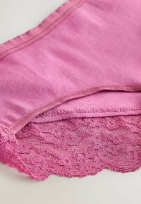Sous-vêtements féminins roses doux avec un détail en dentelle le long du bord inférieur, exposés sur une surface claire.