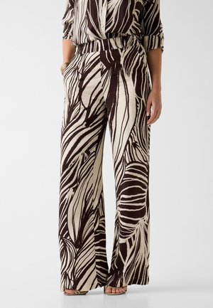 Pantaloni a gamba larga con stampa astratta a zebra bianca e nera, indossati con camicia abbinata e sandali aperti.