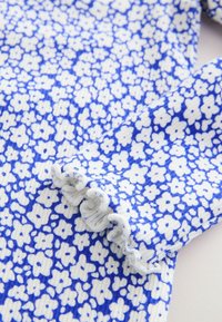 Kék-fehér virágmintás szövet texturált felülettel. Az ujjú végén fodros szegély díszíti, kiemelve a finom mintát.