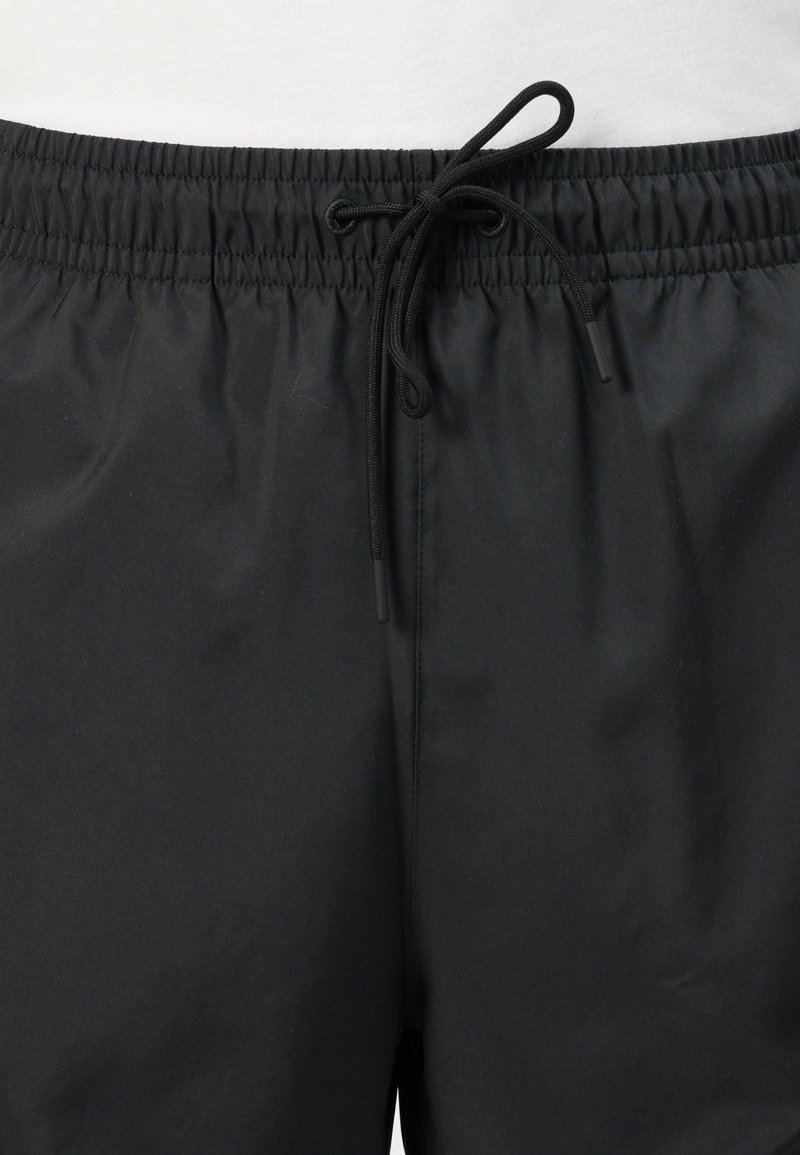 Shorts de bain noirs avec une taille élastique, une texture froncée et un cordon de serrage réglable. Tissu lisse sans motifs ni accents visibles.