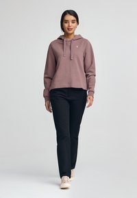 Sudadera morada con cordones y logo, combinada con pantalones negros y zapatos de color claro. Tejido suave, corte relajado y estilo casual.