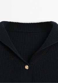 Granatowy sweter z dzianiny z kołnierzem o prążkowanej fakturze i pojedynczym złotym guzikiem przy guziku. Miękka, przyjemna w dotyku tkanina.