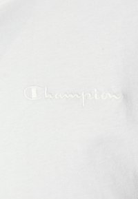 Vit bomullströja med en texturerad, broderad "Champion"-logga i ljus tråd på bröstet. Slät tyg med en klassisk passform.