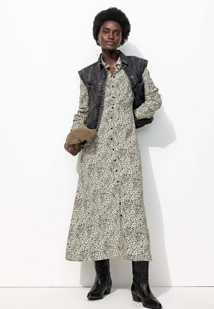 Robe longue à motif noir et blanc avec une taille cintrée. Associée à une veste en denim noire sans manches et des bottes noires jusqu'aux genoux.