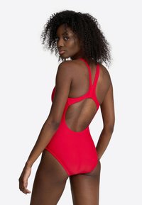 Red one-piece swimsuit with a racerback design, featuring a cutout back. Smooth texture, simple lines, and a fitted silhouette.