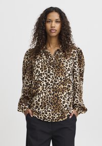 Blouse en imprimé léopard en tissu doux, avec un col, des manches longues et une coupe décontractée. La palette de couleurs comprend du beige, du noir et de l'ivoire.
