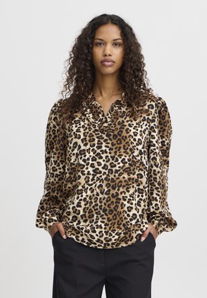 Blouse en imprimé léopard en tissu doux, avec un col, des manches longues et une coupe décontractée. La palette de couleurs comprend du beige, du noir et de l'ivoire.