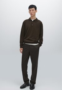 Brown long-sleeve polo with a collar and three buttons, paired with dark brown trousers and black shoes. Smooth fabric, relaxed fit.